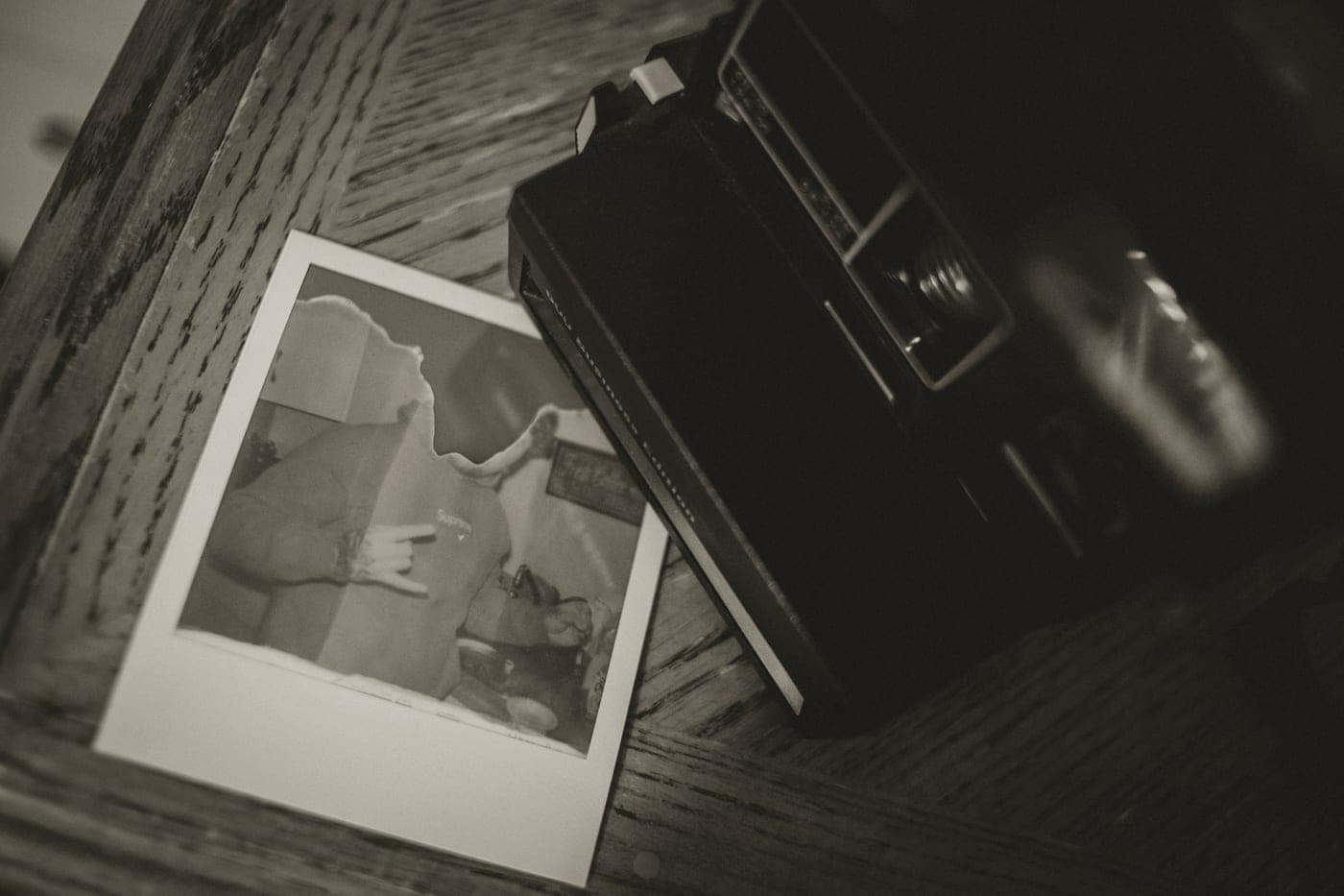 An instant camera resting on a wooden surface beside a developing print