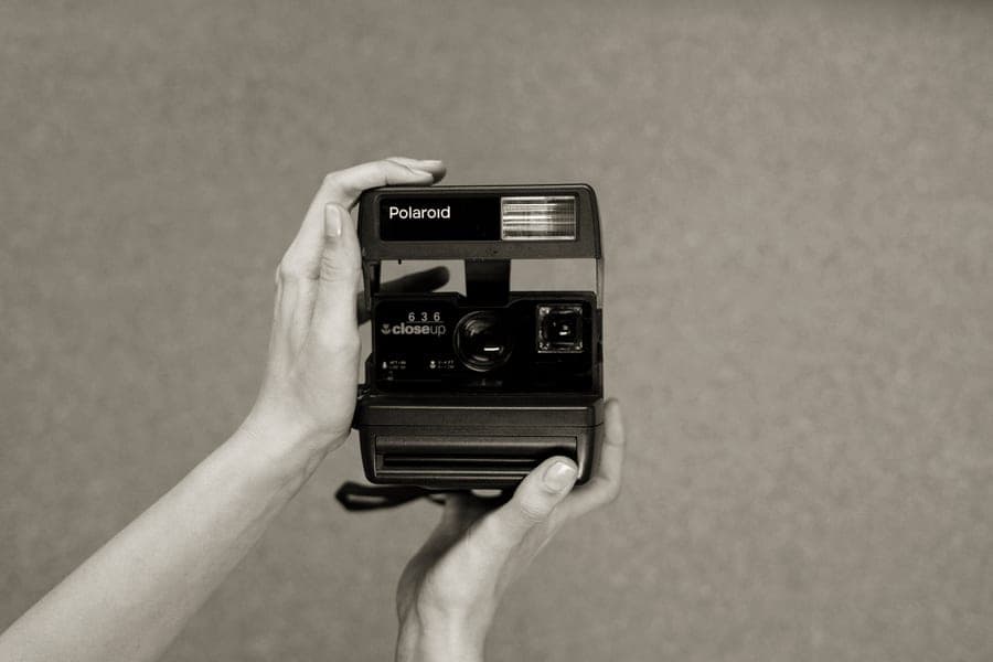 A compact instax-style instant camera resting on a wooden table beside a film pack